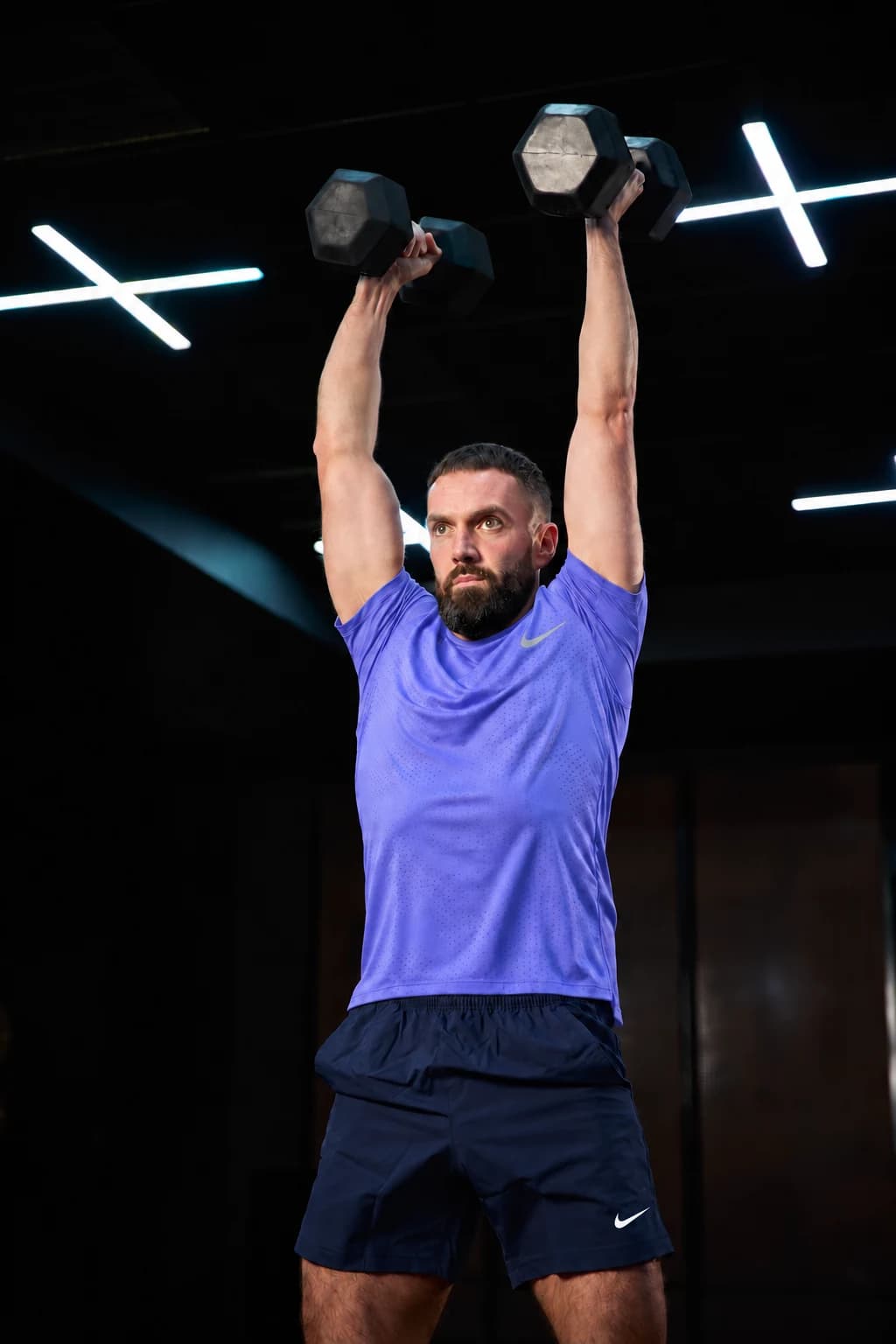 Paul holding dumbbells overhead during a strength session